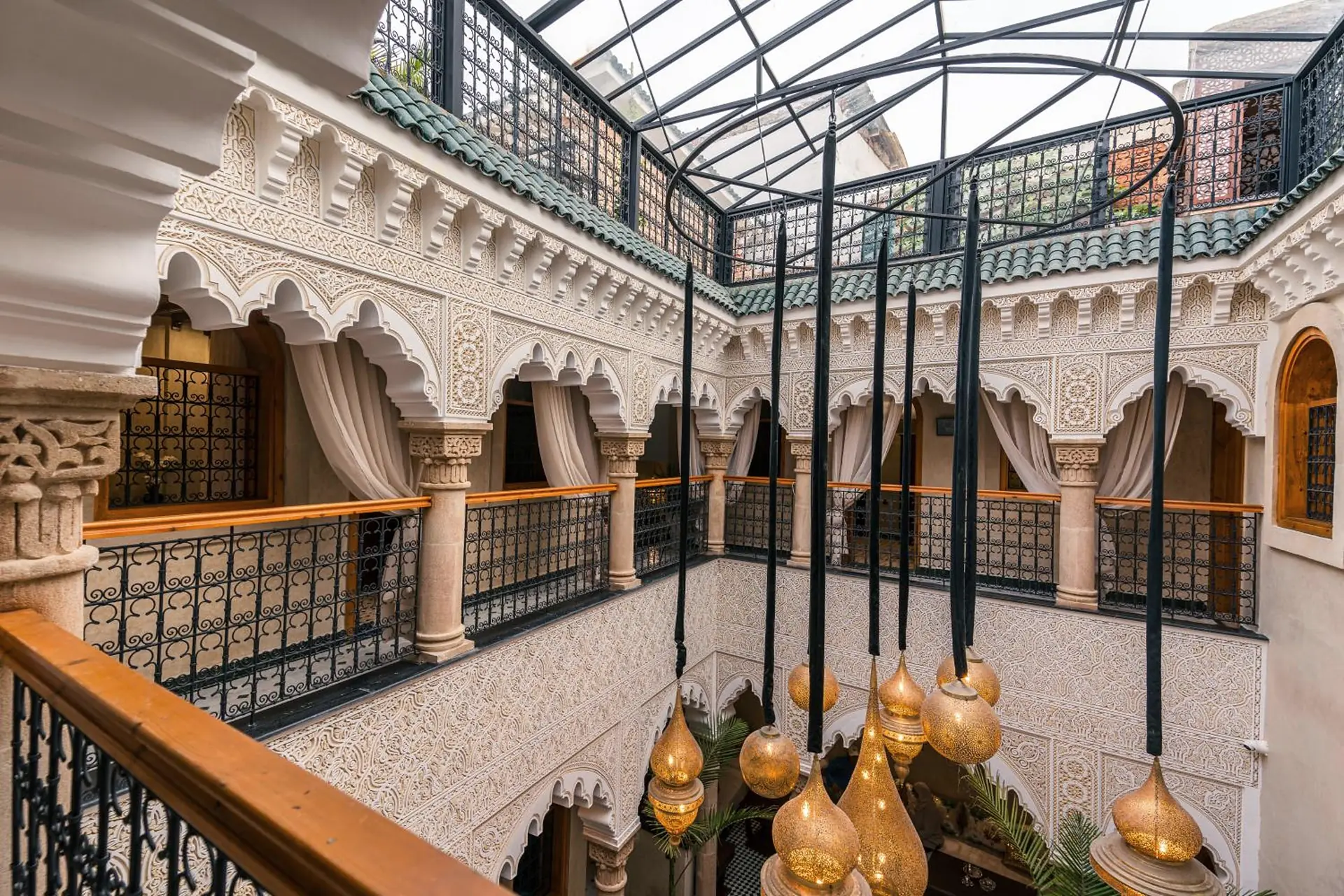 Le patio vu de la galerie : les arcs de plâtre sculpté, la verrière et les lanternes de laiton